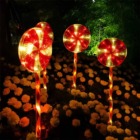 Pirulito de Natal para jardim aceso entre flores amarelas à noite, com disco listrado