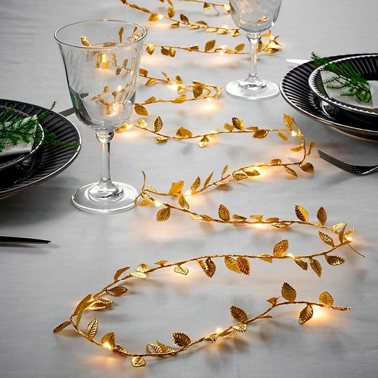 Fio de LED a pilha com folhas douradas acesas sobre uma mesa posta