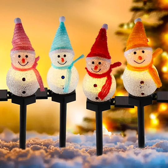 Quatro bonecos de neve solares com gorro e cachecol coloridos, acesos sobre a neve