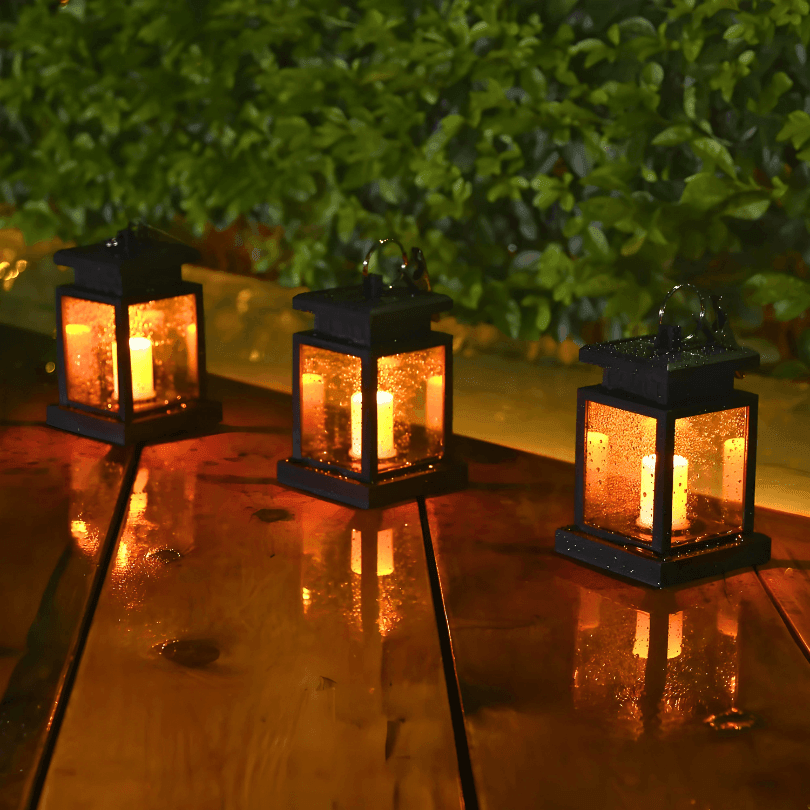 Três lanternas acesas sobre tábuas molhadas de um deck, com luz amarelada nas laterais