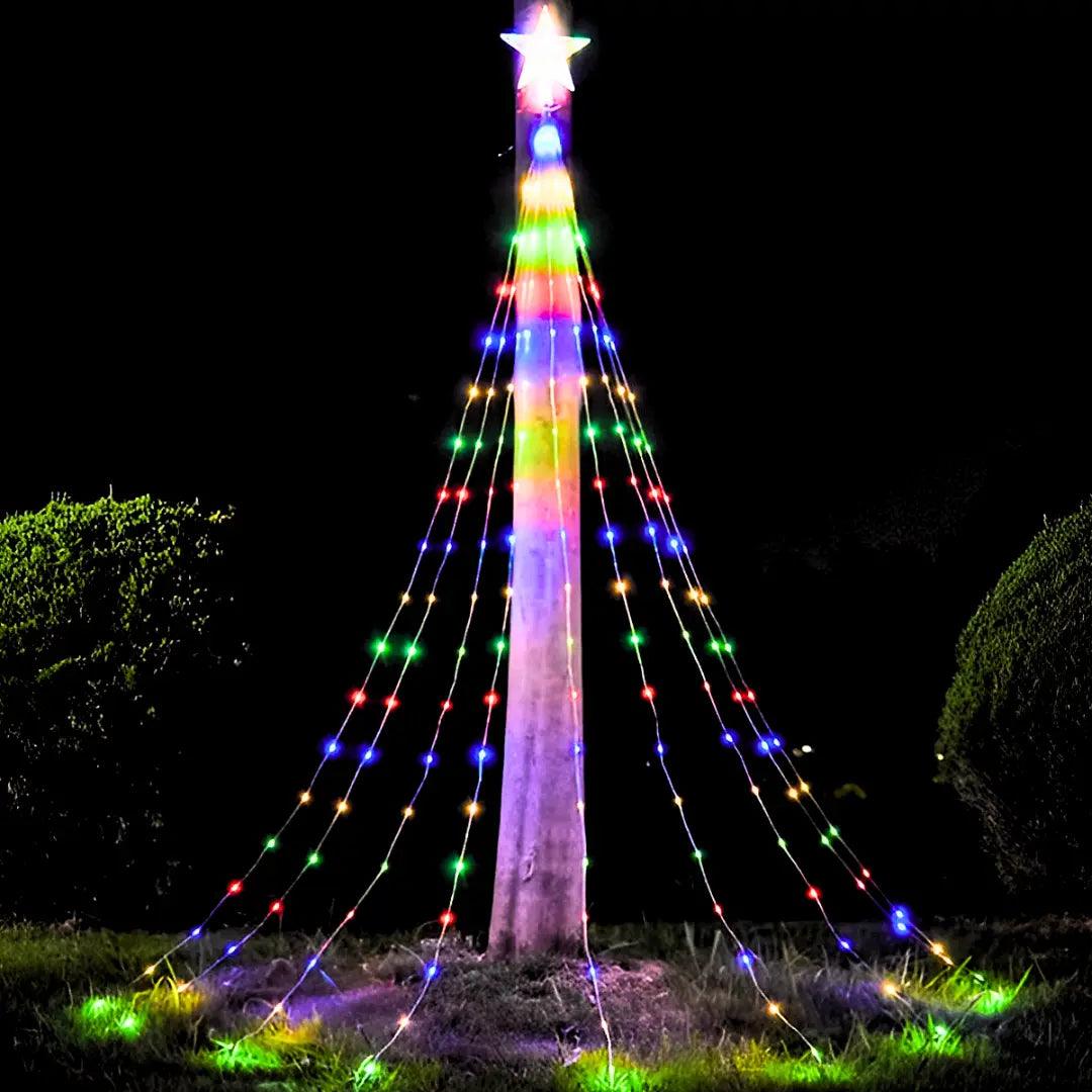 Fios de luz multicolorida descendo do alto de um tronco, sobre o gramado, à noite