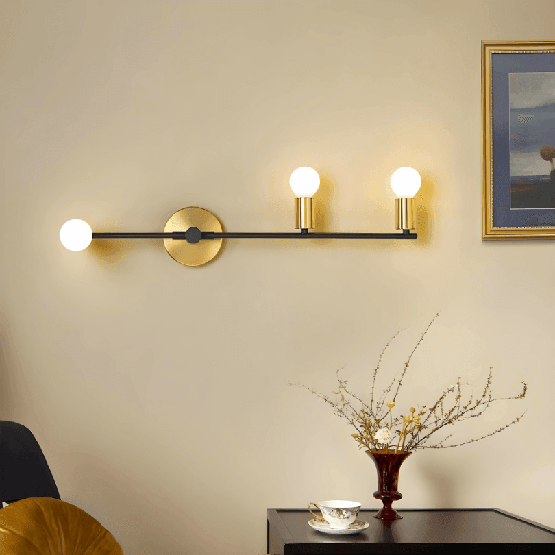 Arandela preta e dourada na horizontal sobre uma mesa com vaso, em parede bege