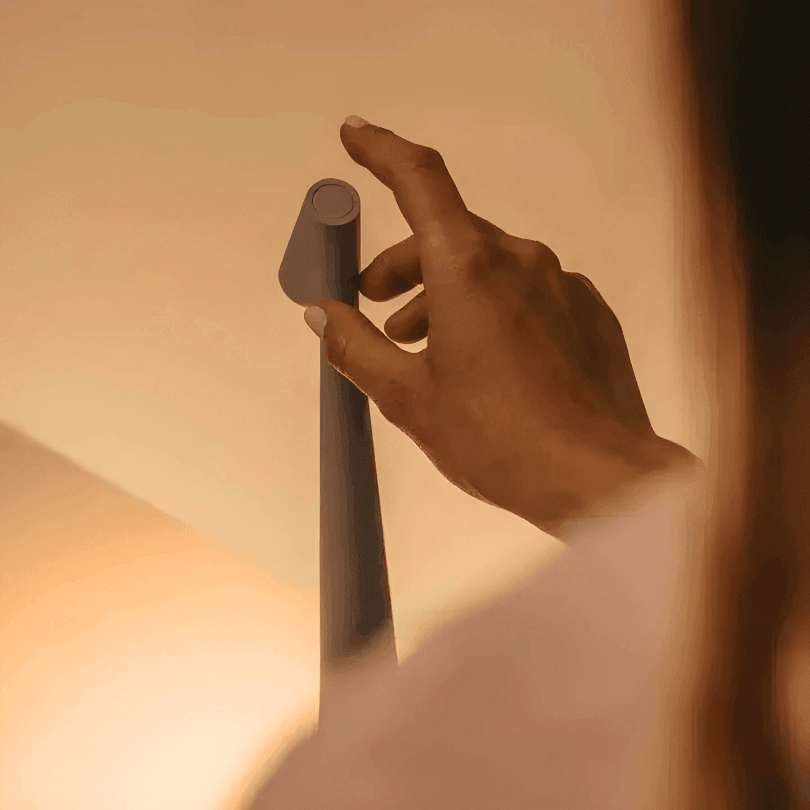 Mão tocando o sensor circular no topo da cabeça da peça cinza, em luz quente