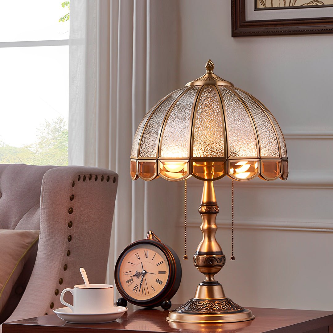 Abajur vintage dourado aceso numa mesa ao lado da poltrona, com relógio e xícara