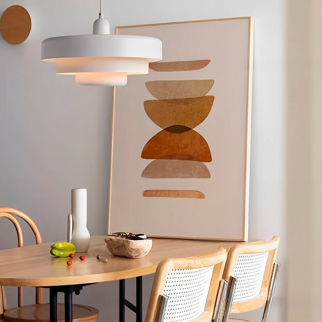 Pendente colorido branco de três níveis aceso sobre mesa de madeira, perto de um quadro