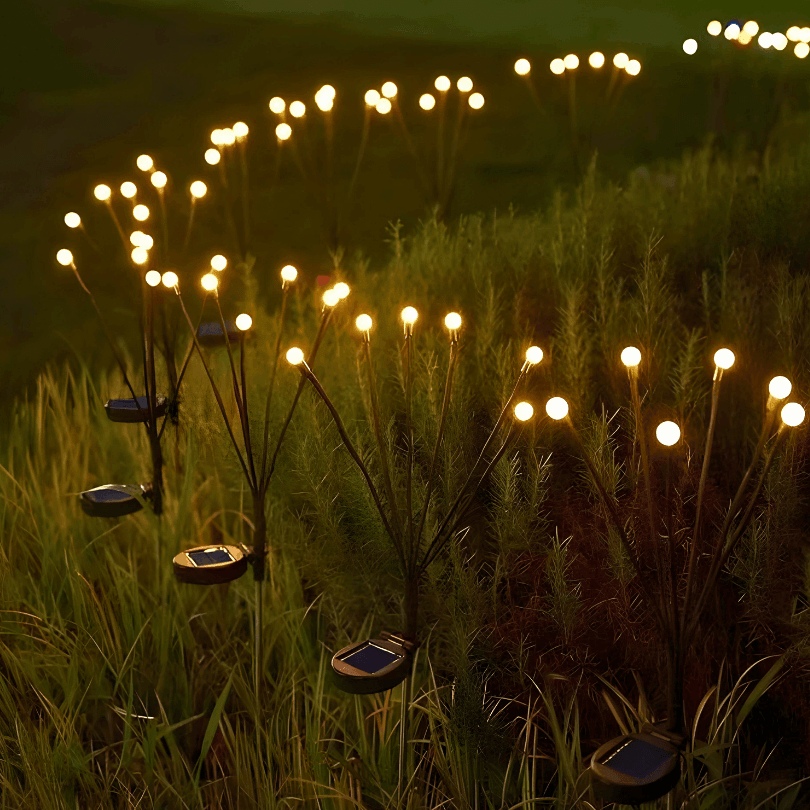 Várias luminárias vagalume acesas num gramado à noite, com os painéis solares junto ao chão