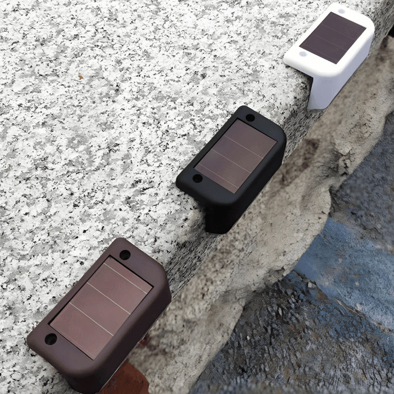 Luminárias solares em preto, marrom e branco sobre a borda de uma mureta de granito