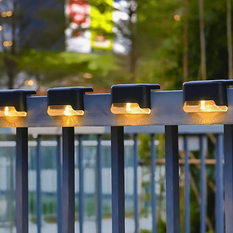 Luminárias solares de luz quente na borda de um deck, com árvores desfocadas ao fundo