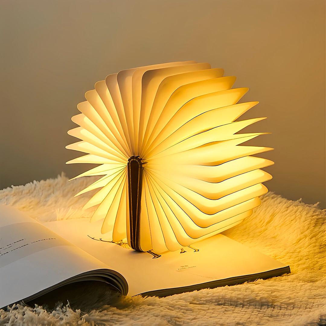Luminária livro aberta em círculo completo e acesa sobre um livro