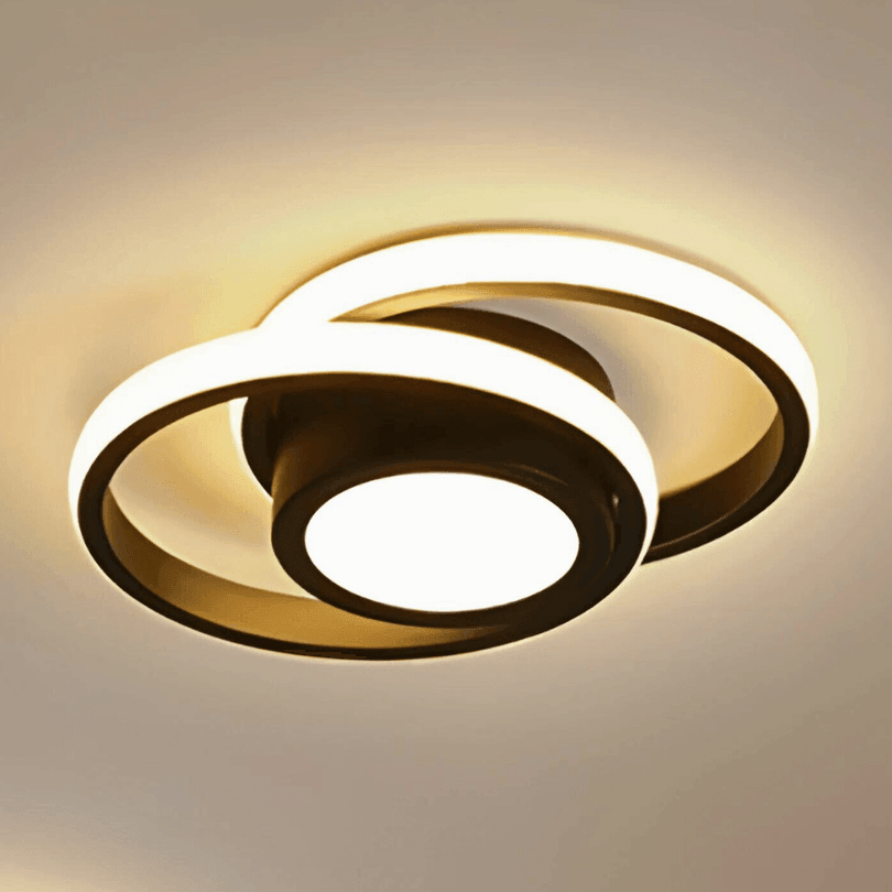 Plafon redondo de LED preto aceso em luz quente, com dois aros sobrepostos no teto