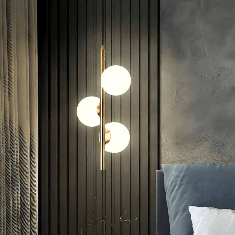 Pendente de três globos acesos ao lado de uma cama, com painel escuro ao fundo