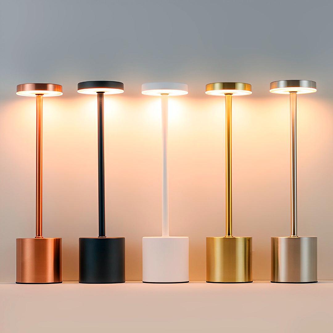 Cinco luminárias acesas lado a lado, em cobre, preto, branco, dourado e prata
