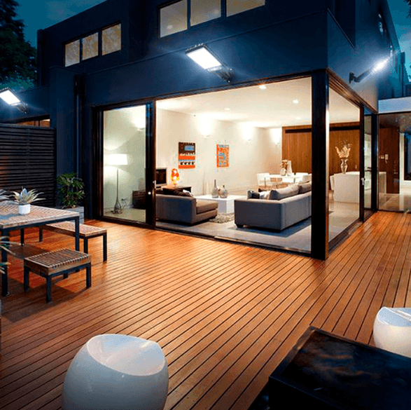 Refletor solar preso na parede alta de uma casa, com sala iluminada ao fundo