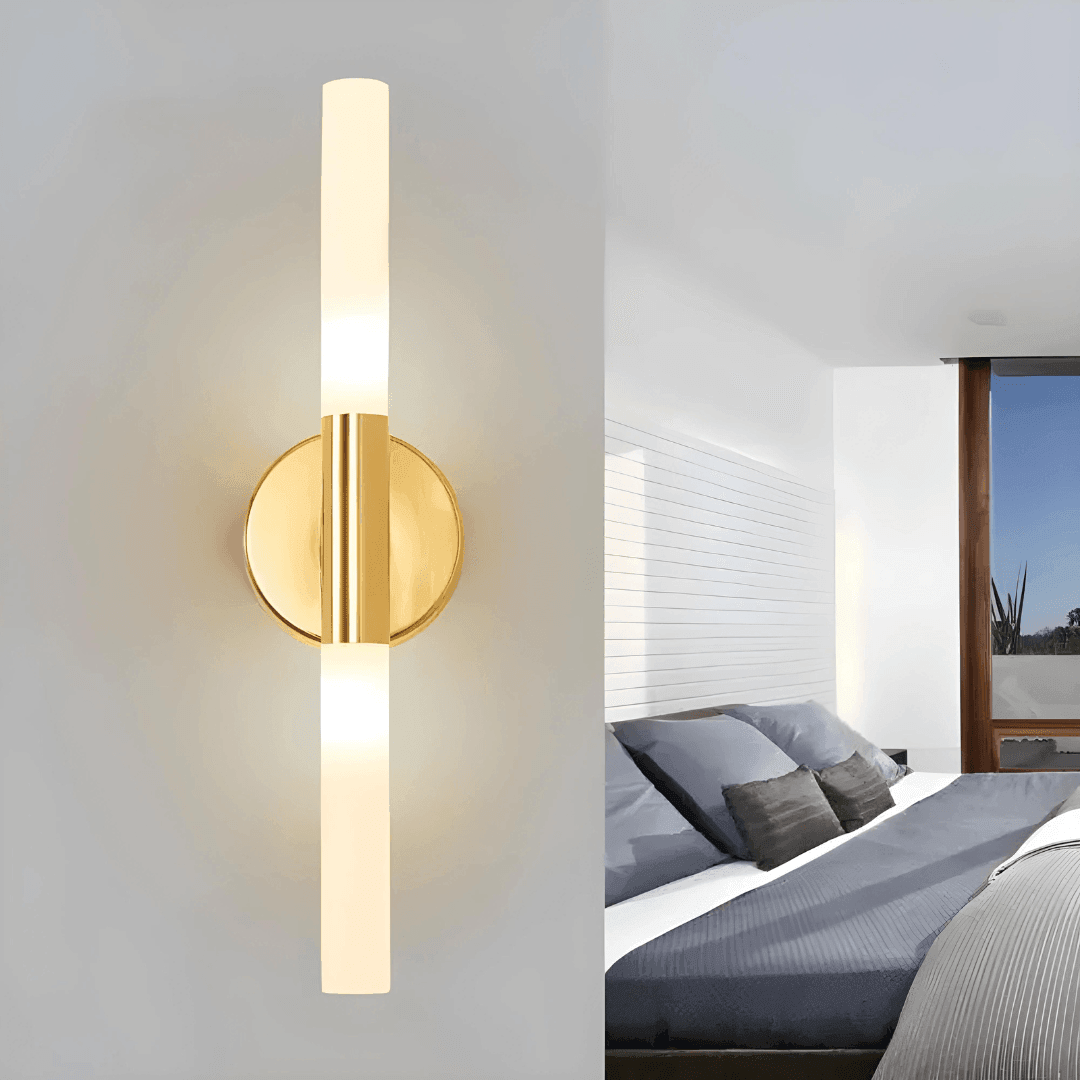 Arandela dourada acesa em luz amarela, com a placa redonda e um quarto ao fundo