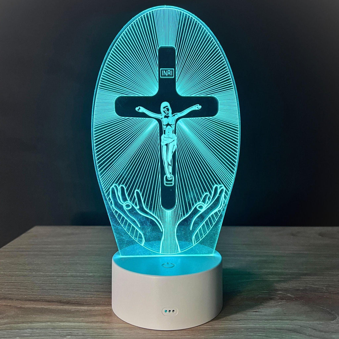 Crucifixo iluminado em azul-turquesa, com Cristo na cruz, raios e mãos abertas sobre base branca