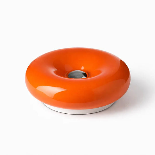 Luminária donut de vidro laranja com centro cromado, sobre fundo branco