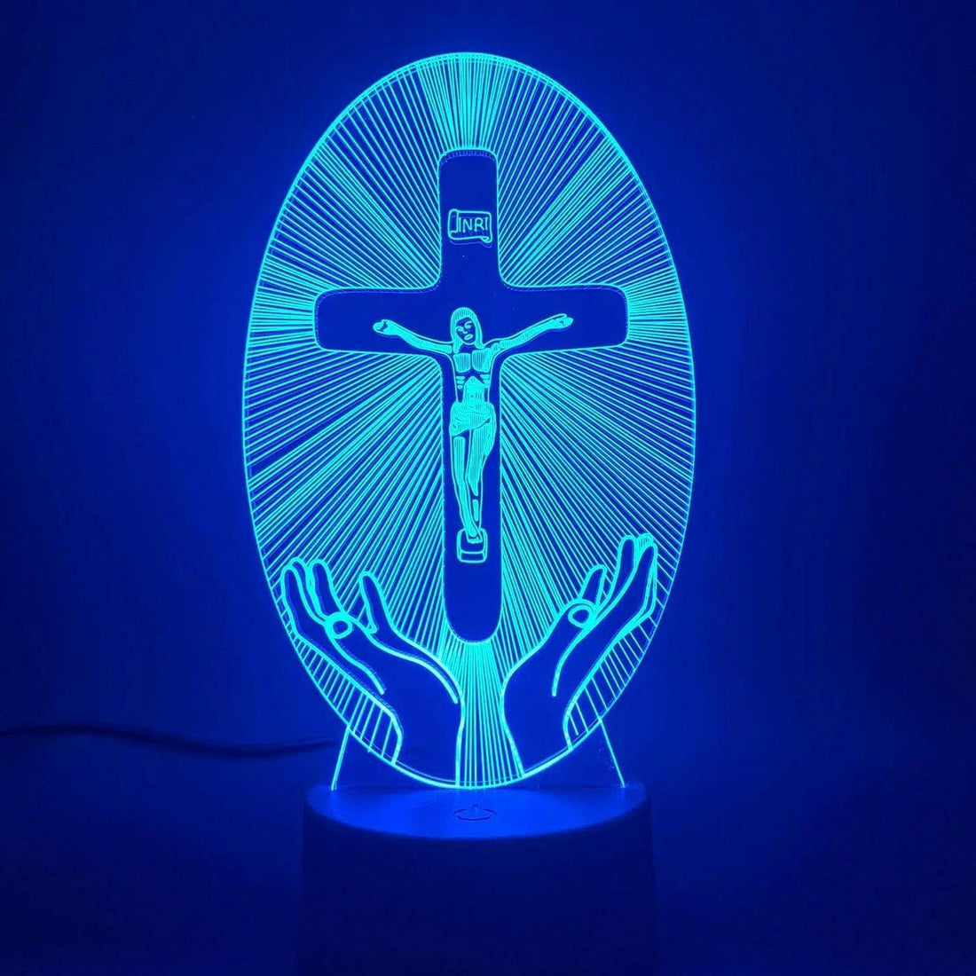 Painel aceso em azul forte sobre fundo azul, com Cristo na cruz e mãos abertas
