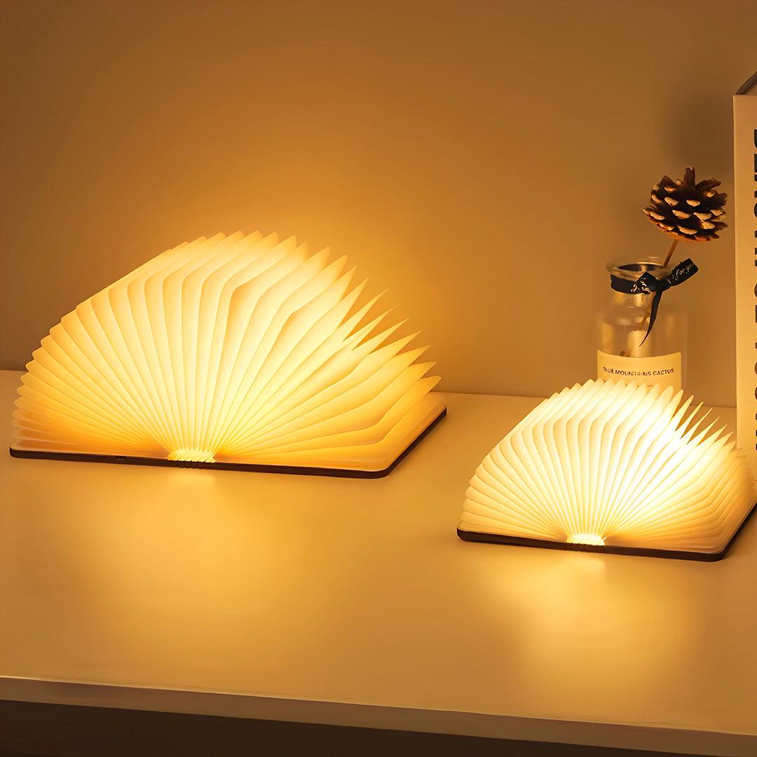 Os dois tamanhos da luminária livro acesos lado a lado sobre a mesa