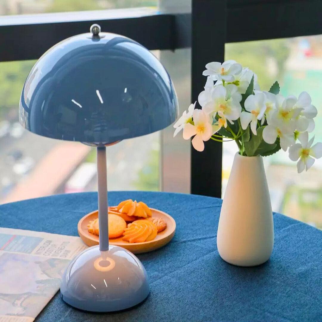 Abajur azul claro sobre toalha azul, perto de biscoitos e de um vaso de flores