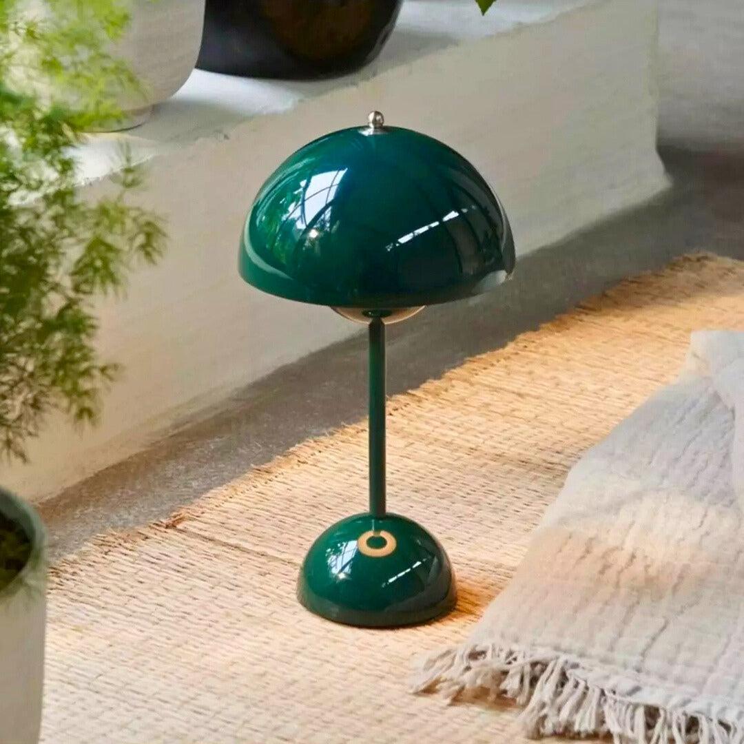 Abajur verde escuro sobre tapete de fibra natural, perto de plantas e de uma manta