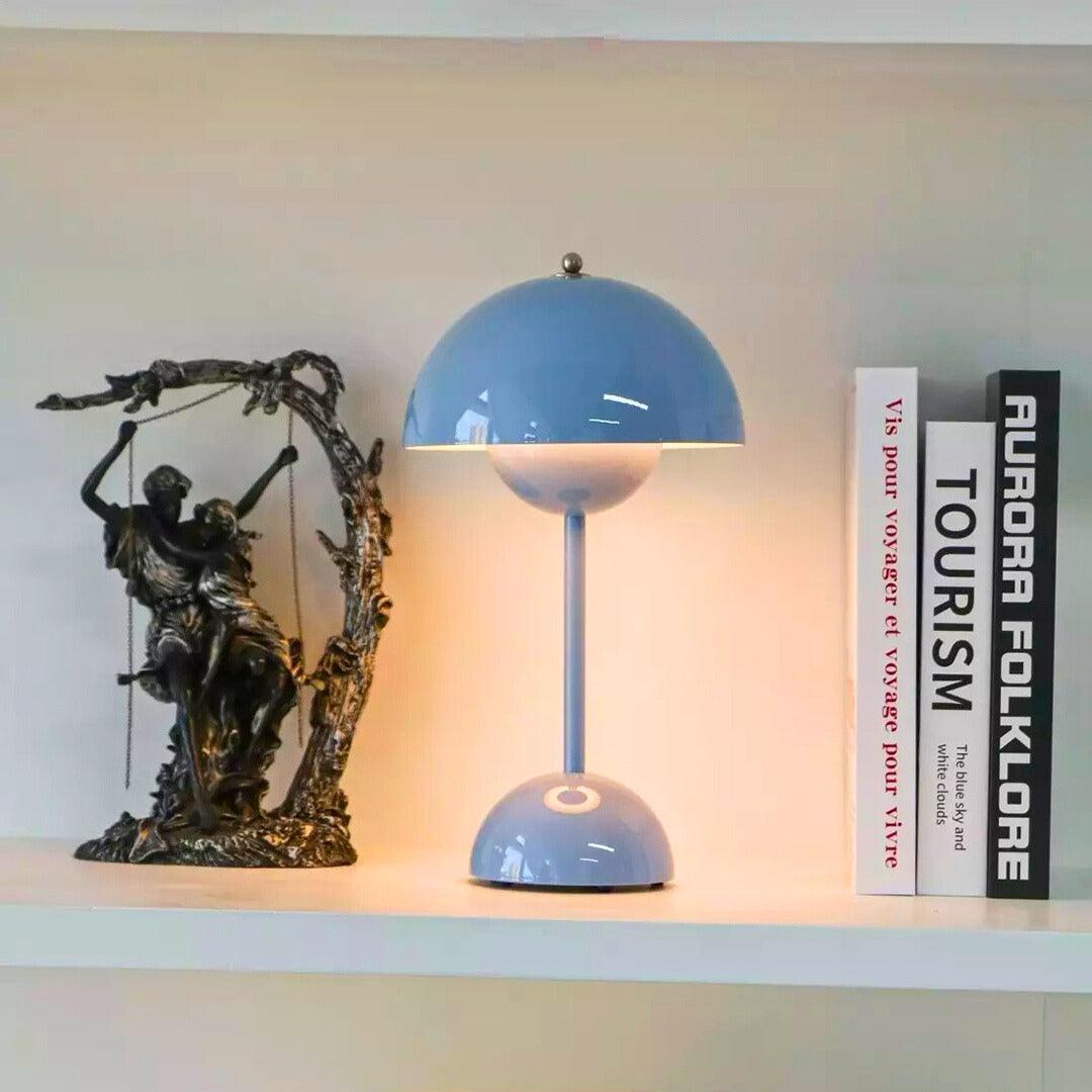 Abajur azul claro aceso numa estante, ao lado de uma escultura e de livros