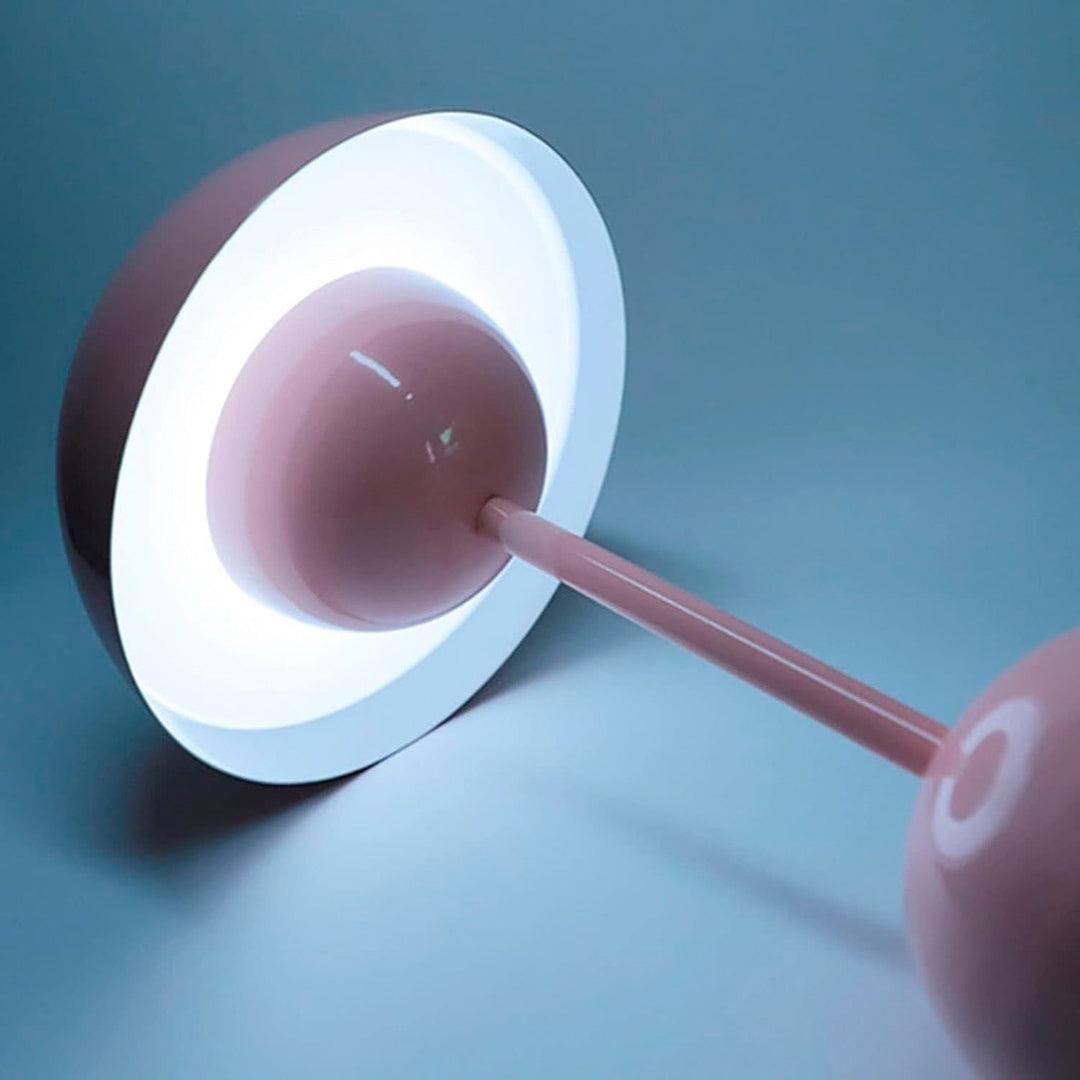 Abajur rosa deitado, com anel de luz branca sob a cúpula em volta da esfera