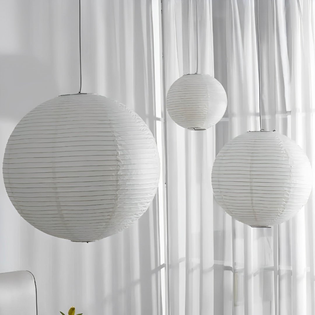 Três esferas de papel apagadas, em tamanhos diferentes, diante de cortinas brancas