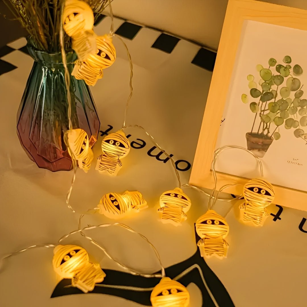 Múmias acesas sobre um tecido bege, perto de um vaso de vidro e um quadro