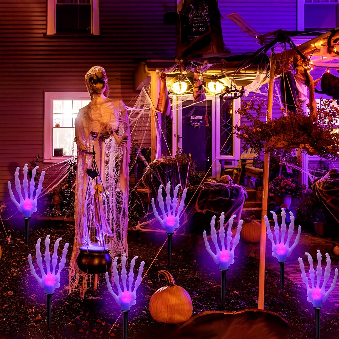 Mão de esqueleto Halloween com luz roxa em espetos solares diante de uma casa decorada