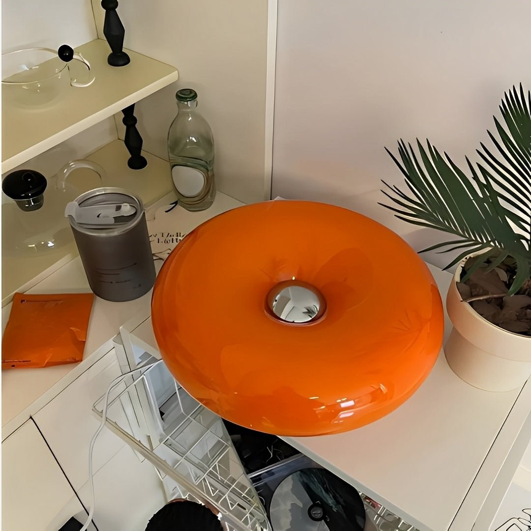 Luminária donut laranja vista de cima sobre bancada, com vasos e planta
