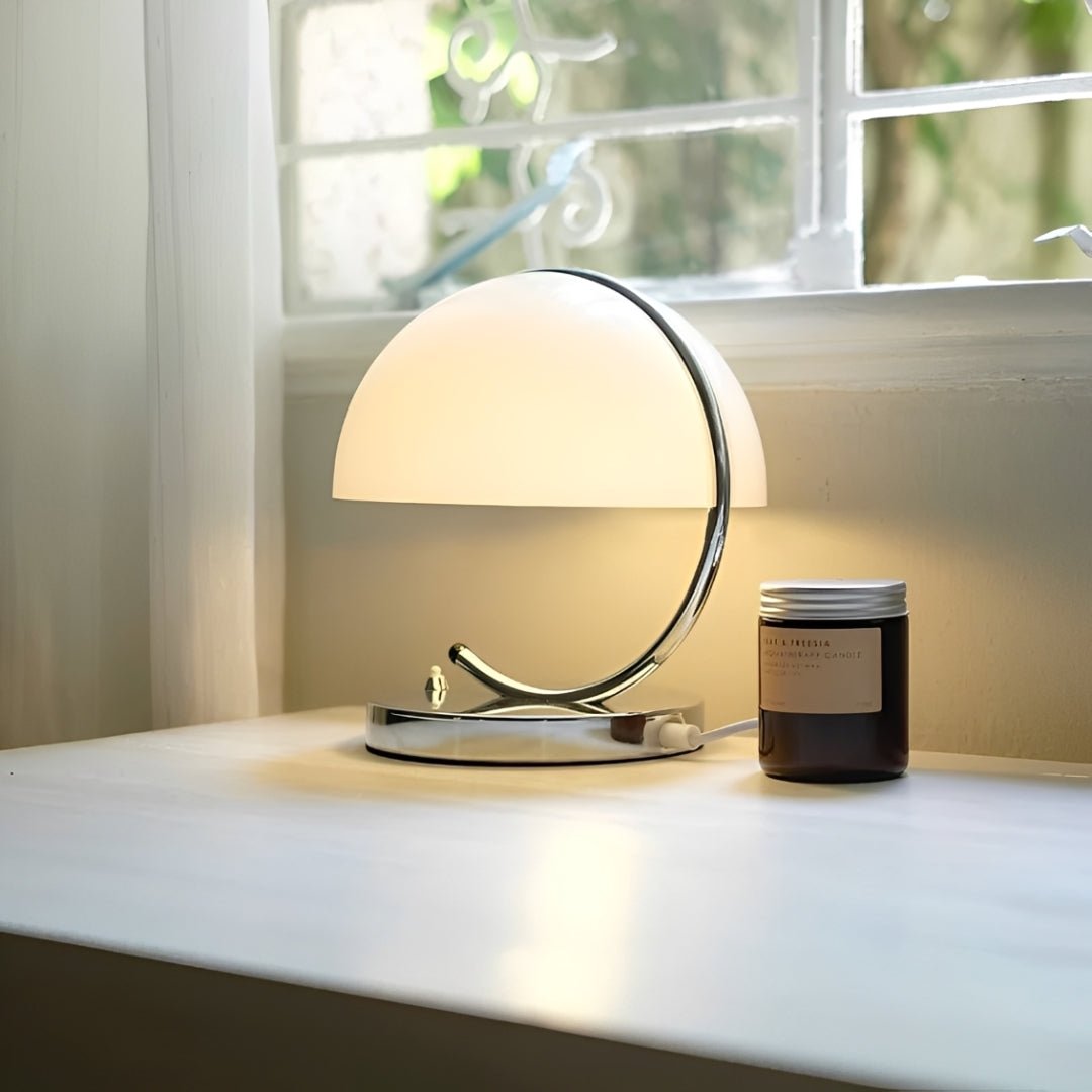Abajur de cúpula branca acesa sobre uma mesa junto à janela, com luz suave
