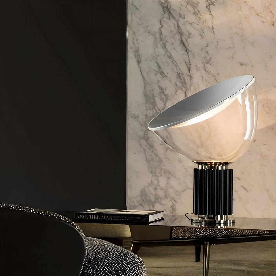 Luminária de base preta acesa sobre mesa de centro, diante de parede de mármore