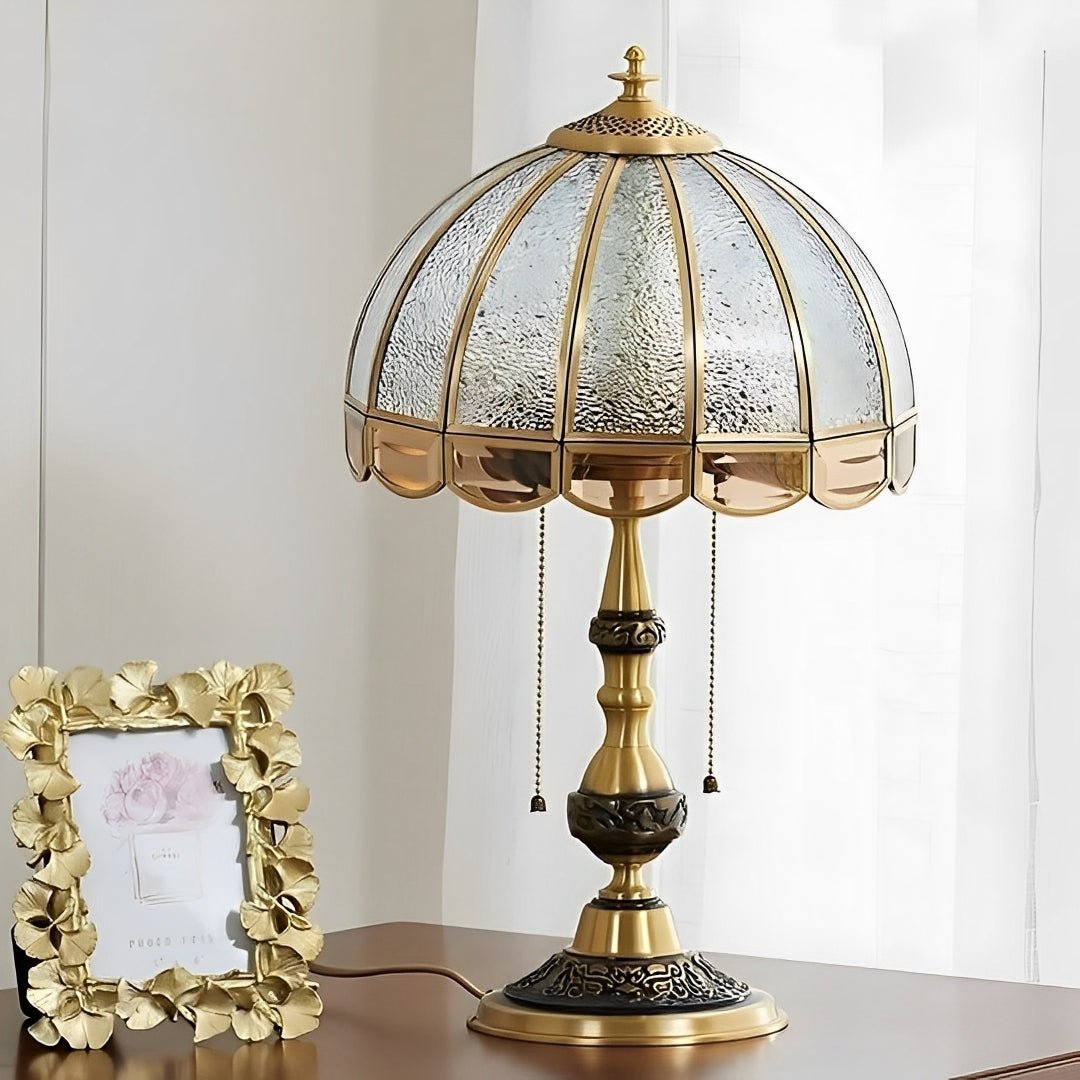 Abajur dourado aceso sobre uma cômoda branca, ao lado de um porta-retratos dourado