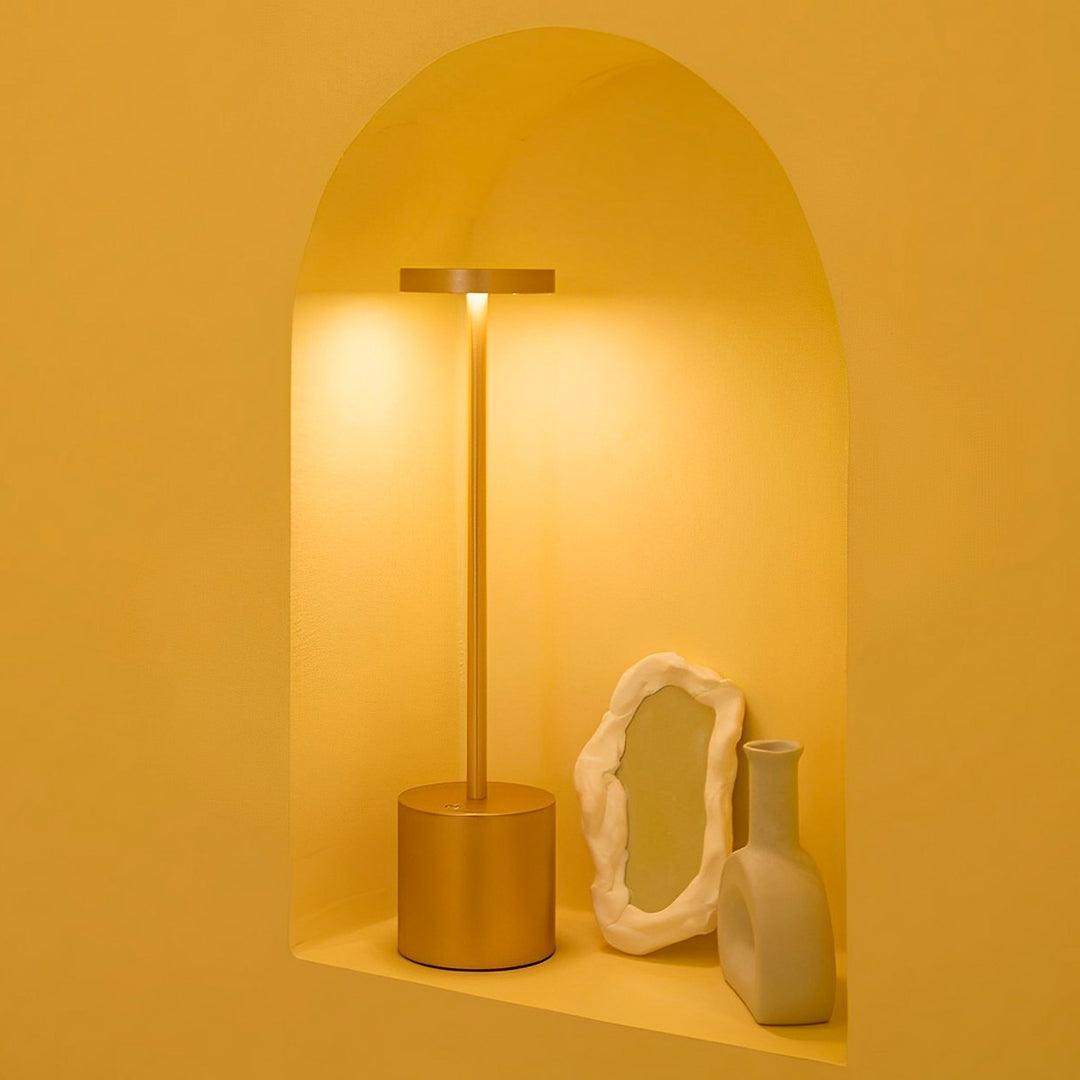 Luminária dourada acesa num nicho arqueado de parede amarela, com porta-retrato e vaso