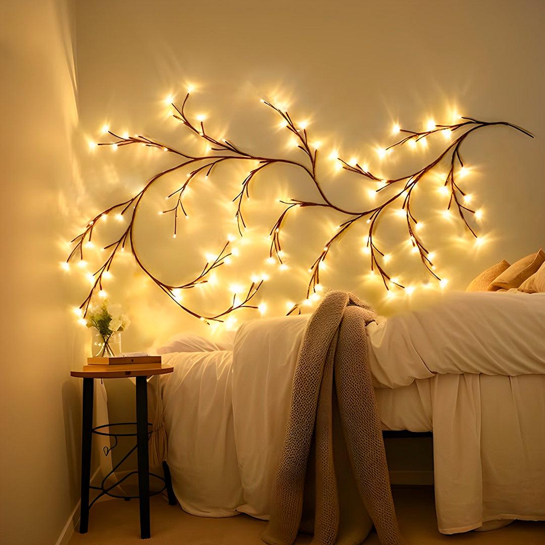 Galhos de LED acesos na parede acima de uma cama, com banqueta ao lado
