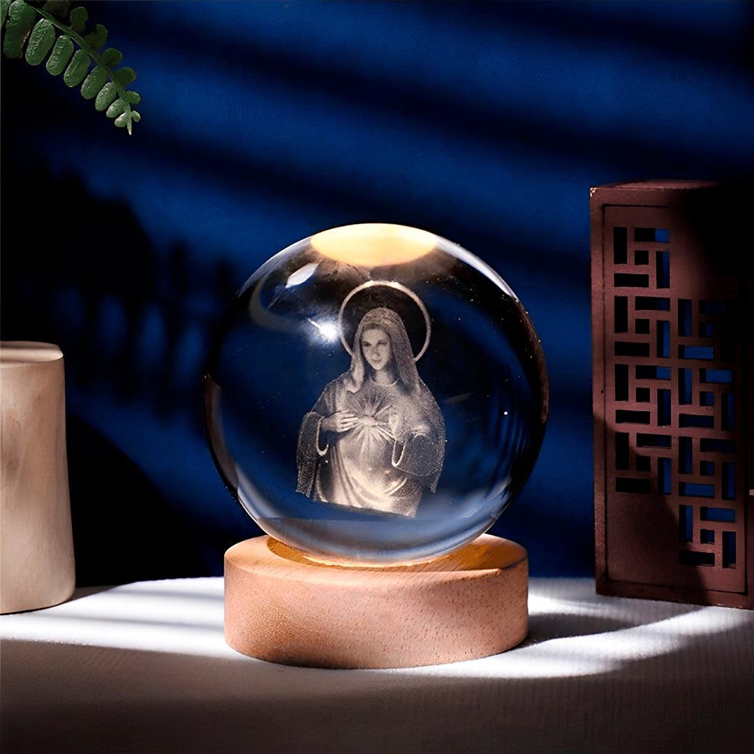 Luminária Virgem Maria em bola de cristal sobre base de madeira, acesa com luz quente
