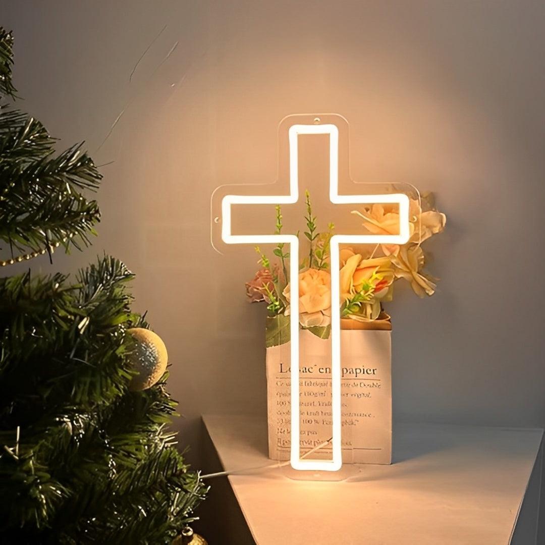 Cruz de neon acesa numa prateleira, com flores atrás e um pinheiro ao lado