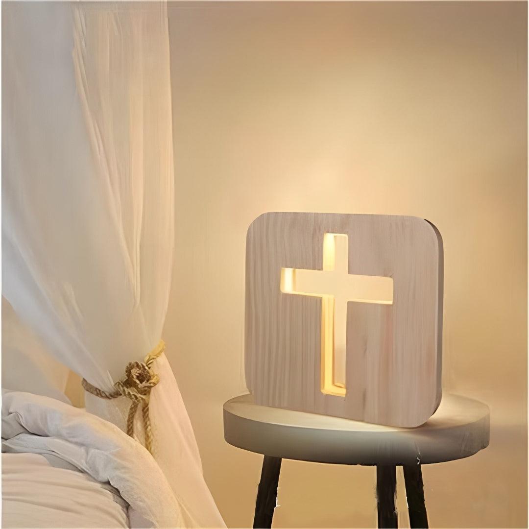 Cruz de madeira com LED acesa em branco quente sobre um banco, junto à cama