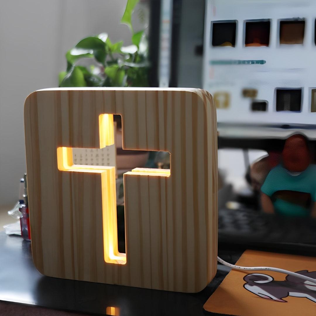 Cruz de madeira acesa sobre uma mesa de trabalho, com planta e computador ao fundo
