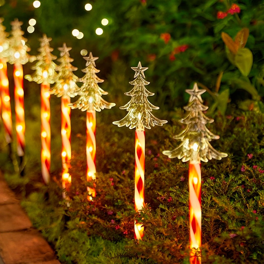 Espetos de Natal modelo árvore acesos em fileira ao lado de um canteiro à noite