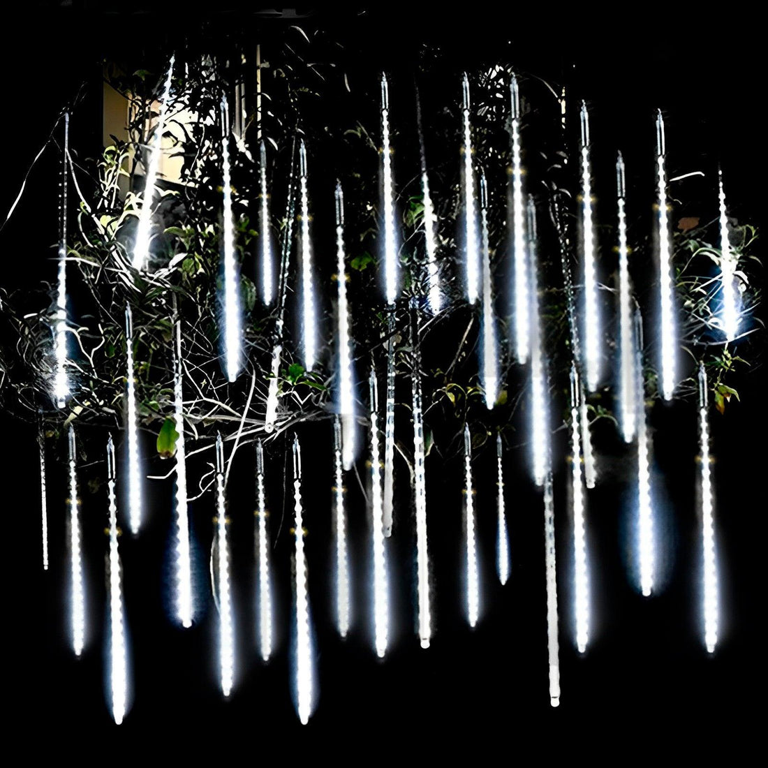 Tubos de luz branca pendurados nos galhos de uma árvore, acesos à noite