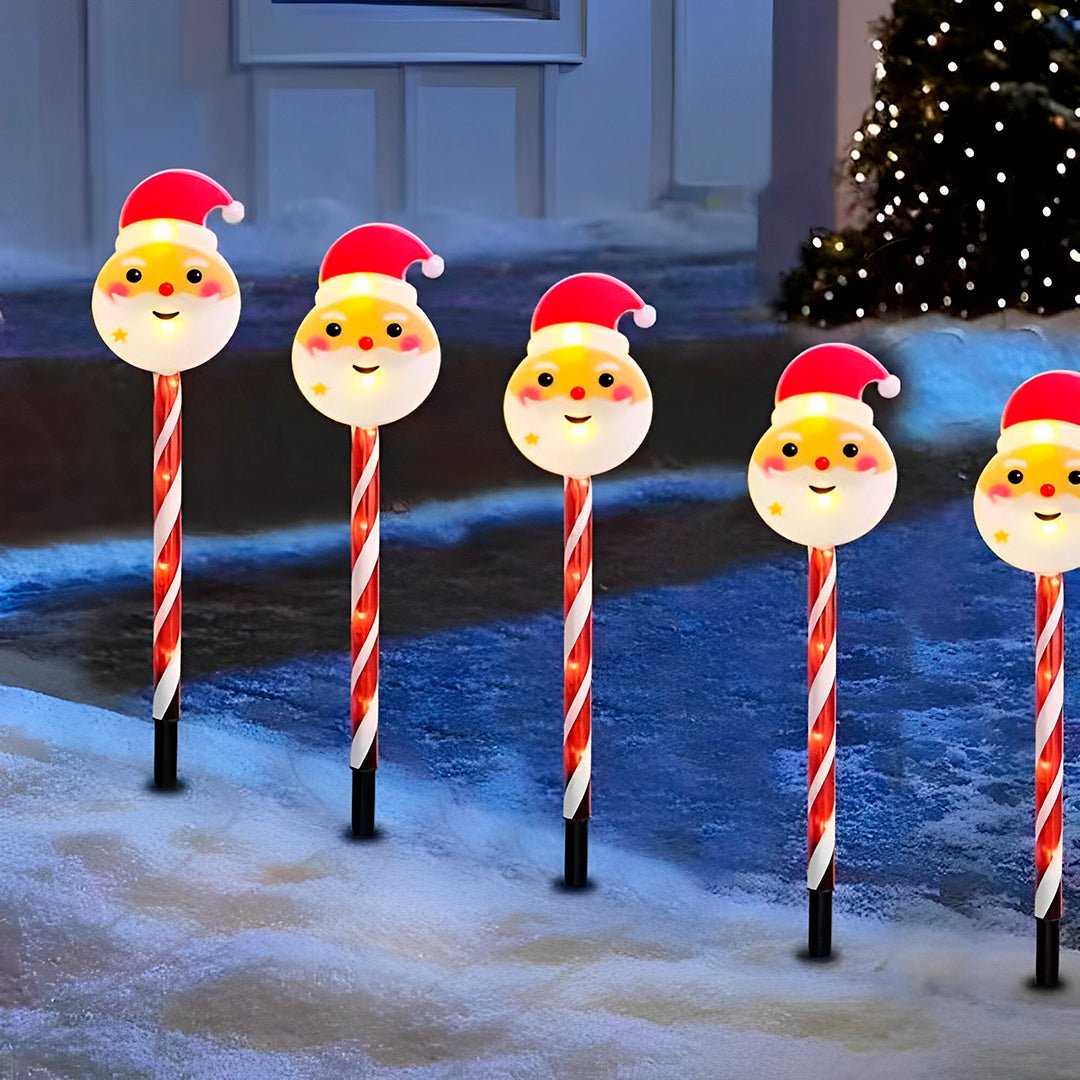 Cinco espetos modelo Papai Noel acesos em fileira diante de uma porta com neve