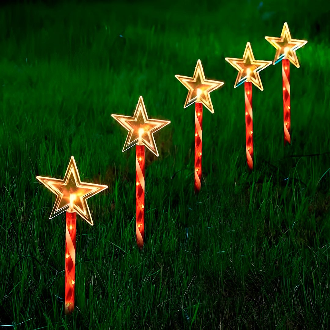 Estrelas acesas em luz quente sobre hastes vermelhas, em diagonal num gramado à noite