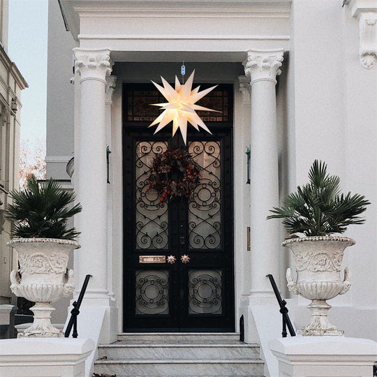 Estrela de Natal iluminada de muitas pontas, pendurada na porta de entrada de uma casa branca