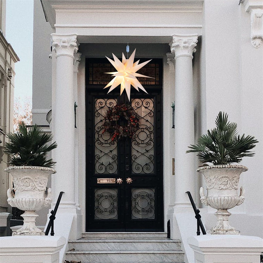 Estrela de Natal iluminada de muitas pontas, pendurada na porta de entrada de uma casa branca