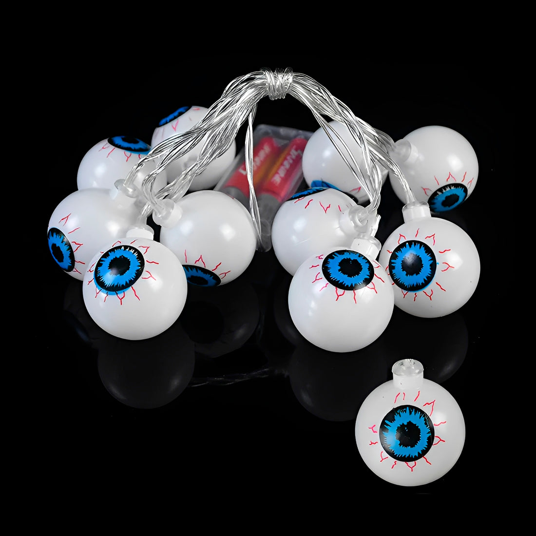 Varal de olhos com um olho solto, sobre fundo preto, com caixa de pilhas