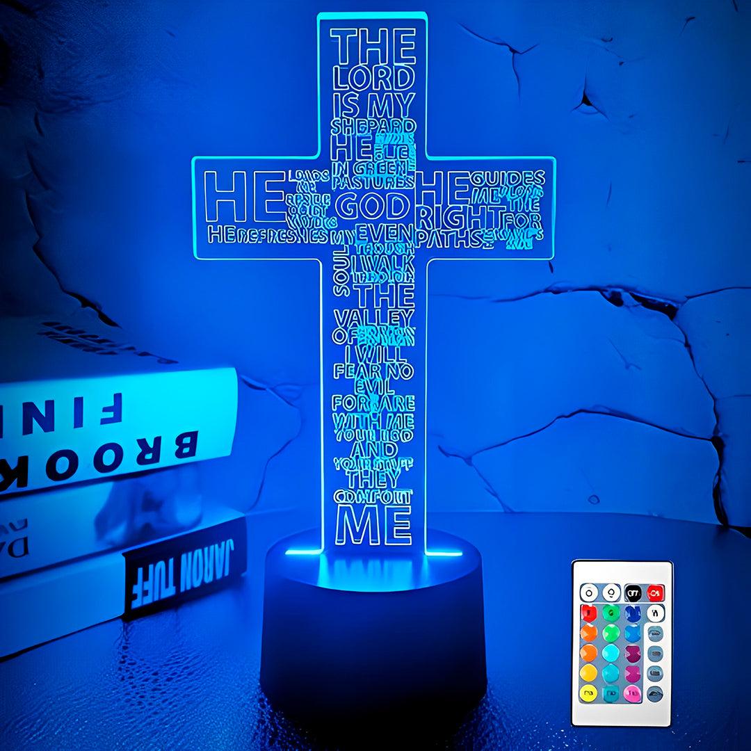 Luminária cruz com versículo acesa em azul, ao lado de livros e do controle remoto