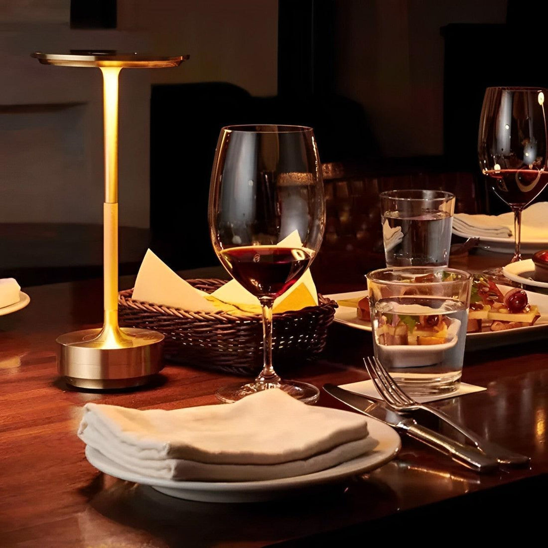 Peça dourada acesa sobre mesa com taças de vinho, pratos e guardanapo, em ambiente escuro