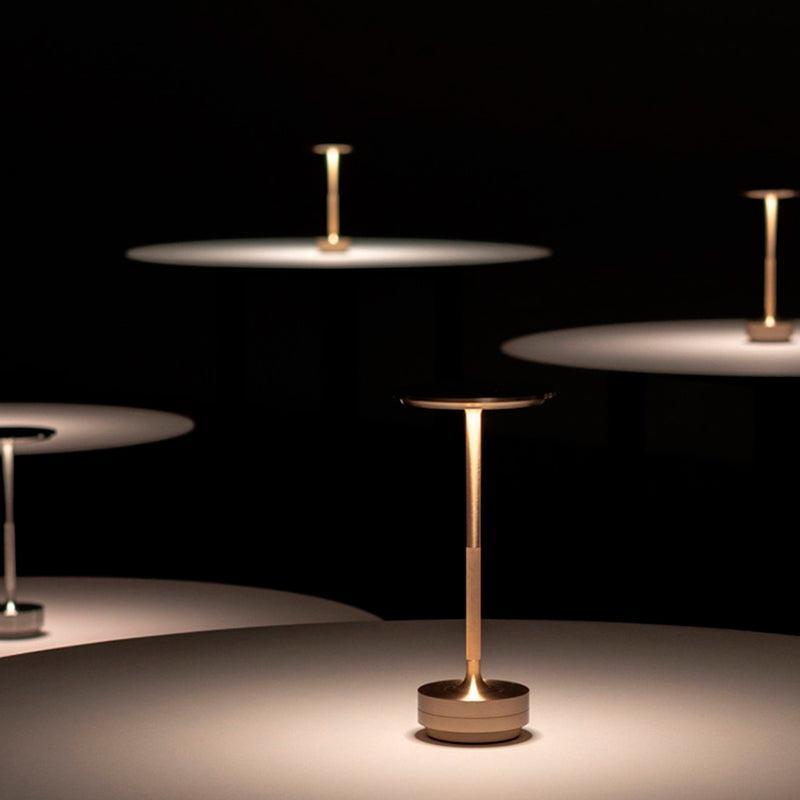 Várias peças de disco fino acesas na penumbra, com a luz espalhada sobre mesas escuras