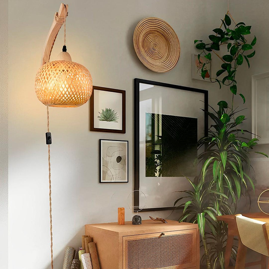 Arandela de bambu com tomada acesa no canto, ao lado de quadros, plantas e aparador